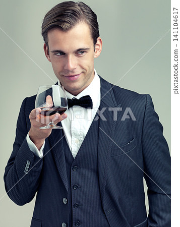Glass, whiskey and young gentleman for idea in studio, happy and vintage fashion by white background. Alcohol, drinking and man in retro suit or tuxedo, bow tie and relax in smile at formal event Glass, whiskey and young gentleman for idea in studio, happy and vintage fashion by white background. Alcohol, drinking and man in retro suit or tuxedo, bow tie and relax in smile at formal event 141104617