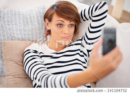 Woman, selfie and funny or relax on sofa for silly communication and social media at home. Young person on couch in living room on mobile or internet for profile picture, tongue and face or emoji Woman, selfie and funny or relax on sofa for silly communication and social media at home. Young person on couch in living room on mobile or internet for profile picture, tongue and face or emoji 141104732
