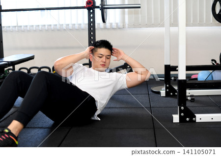 A young Asian man doing sit-ups at the gym. A young Asian man doing sit-ups at the gym. 141105071