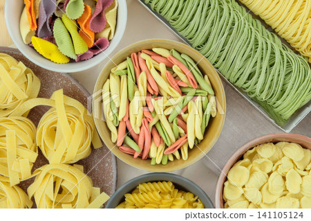 Variety of multi-colored pasta. Uncooked pasta on ceramic plate. Pattern of gastronomy. Top view. Variety of multi-colored pasta. Uncooked pasta on ceramic plate. Pattern of gastronomy. Top view. 141105124