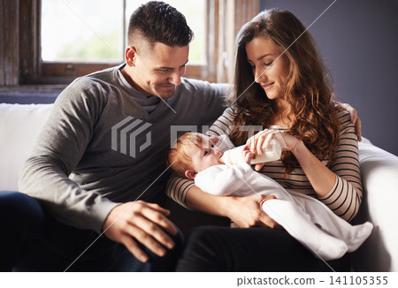 Mother, baby and milk feeding with dad in a family home with love, support and care together. Smile, relax and bottle for youth development and growth with mom and father on a living room sofa Mother, baby and milk feeding with dad in a family home with love, support and care together. Smile, relax and bottle for youth development and growth with mom and father on a living room sofa 141105355