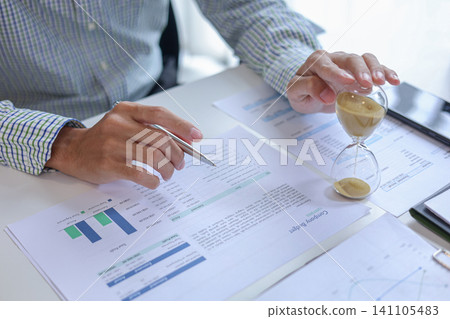 Business accountant reviewing financial charts and data performance in office with hourglass on desk. Time management and financial analysis concept. Business accountant reviewing financial charts and data performance in office with hourglass on desk. Time management and financial analysis concept. 141105483