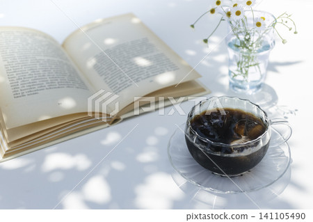 在陽光斑駁的桌旁,一邊享用冰咖啡一邊閱讀,幾束鮮花點綴著夏日生活。 在陽光斑駁的桌旁,一邊享用冰咖啡一邊閱讀,幾束鮮花點綴著夏日生活。 141105490