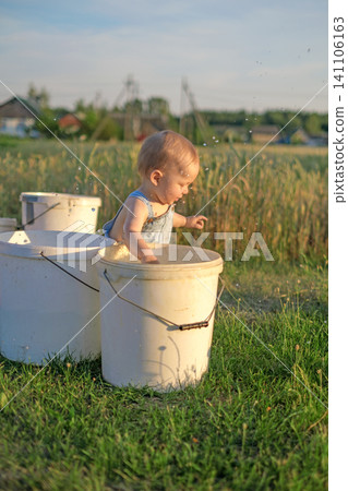 A small child splashing in a bucket of water in the garden. Children's pranks. A small child splashing in a bucket of water in the garden. Children's pranks. 141106163