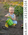 A funny cute baby with a bucket and cucumbers is sitting on the ground in a vegetable garden. Homegrown vegetables without GMOs 141106164