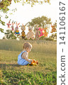 Soft children's toys are hanging to dry on a clothesline, and a baby is sitting on the grass, playing with a stuffed bull. 141106167