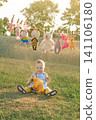 A little one-year-old boy is sitting on the grass in a park, surrounded by a variety of toys that are drying after being washed. 141106180