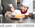 An image of an Asian female pastry chef finishing a cake. 141106608