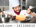 An image of an Asian female pastry chef finishing a cake. 141106610