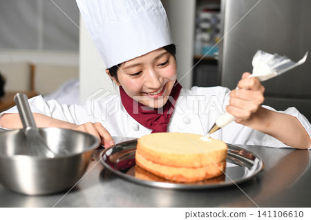 An image of an Asian female pastry chef finishing a cake. 141106610