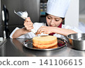 An image of an Asian female pastry chef finishing a cake. 141106615