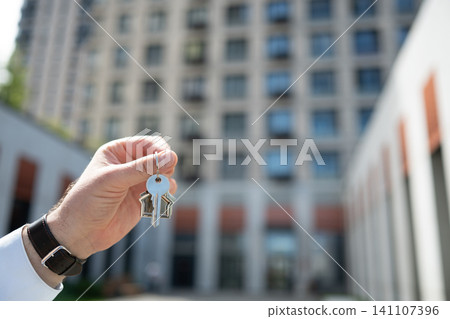 Hand holding house keys against modern apartment building Hand holding house keys against modern apartment building 141107396