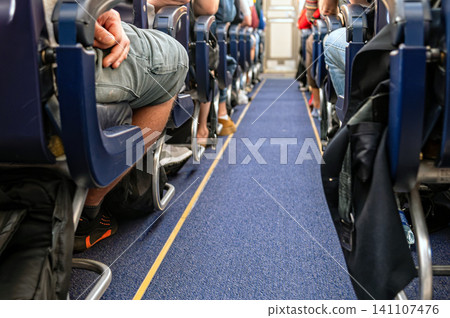 People sit on an airplane with bags under seats during a flight People sit on an airplane with bags under seats during a flight 141107476