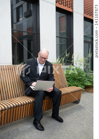 Businessman working on laptop while sitting on outdoor bench 141107873