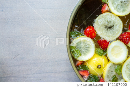Fruit infused water with lemon slices, strawberries, mint leaves, and ice in metal bowl on rustic gray tabletop, top view composition with bright fresh colors and generous copy space Fruit infused water with lemon slices, strawberries, mint leaves, and ice in metal bowl on rustic gray tabletop, top view composition with bright fresh colors and generous copy space 141107900