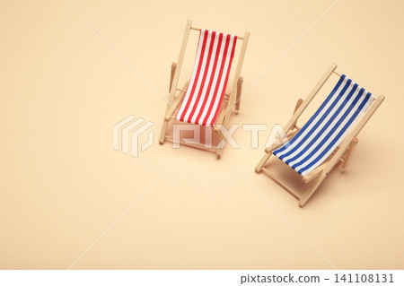 Two miniature deck chairs with red and blue striped canvas seats on beige background. Summer concept. Two miniature deck chairs with red and blue striped canvas seats on beige background. Summer concept. 141108131