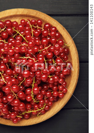 Red currants on wooden plate on black wooden background. Fresh and vibrant food photography for healthy eating. Vertical photo 141108143
