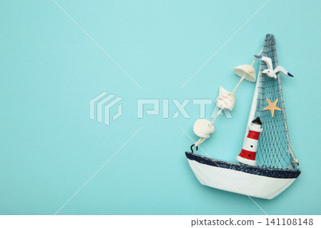 Decorative sailboat ornament with striped lighthouse detail, fabric sail, seashell garland on blue background. Summer concept Decorative sailboat ornament with striped lighthouse detail, fabric sail, seashell garland on blue background. Summer concept 141108148