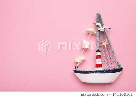 Decorative sailboat ornament with striped lighthouse detail, fabric sail, seashell garland on pink background. Summer concept Decorative sailboat ornament with striped lighthouse detail, fabric sail, seashell garland on pink background. Summer concept 141108161