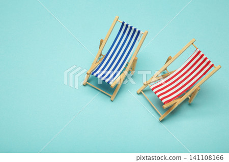 Two miniature deck chairs with red and blue striped canvas seats on blue background. Summer concept. 141108166