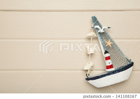 Decorative sailboat ornament with striped lighthouse detail, fabric sail, seashell garland on light background. Summer concept Decorative sailboat ornament with striped lighthouse detail, fabric sail, seashell garland on light background. Summer concept 141108167