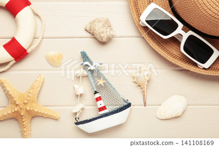 Summer beach flat lay featuring straw sun hat, black sunglasses, seashells, starfish, decorative sailboat and lighthouse accent on light wooden background Summer beach flat lay featuring straw sun hat, black sunglasses, seashells, starfish, decorative sailboat and lighthouse accent on light wooden background 141108169