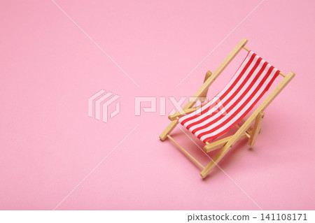 One miniature deck chair with red and blue striped canvas seats on pink background. Summer concept. One miniature deck chair with red and blue striped canvas seats on pink background. Summer concept. 141108171