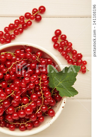 Red currants on white plate on light wooden background. Fresh and vibrant food photography for healthy eating. Vertical photo Red currants on white plate on light wooden background. Fresh and vibrant food photography for healthy eating. Vertical photo 141108196
