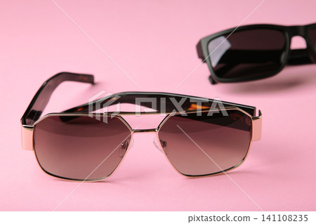 Folded stylish sunglasses on pink background Folded stylish sunglasses on pink background 141108235