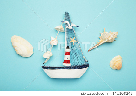 Decorative sailboat ornament with striped lighthouse detail, fabric sail, seashell garland on blue background. Summer concept Decorative sailboat ornament with striped lighthouse detail, fabric sail, seashell garland on blue background. Summer concept 141108245