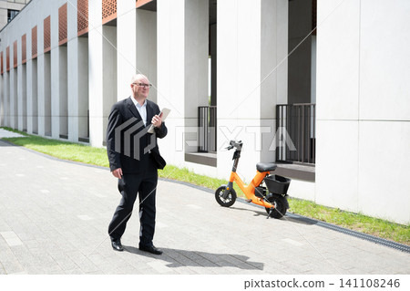 Businessman walking near electric bike outside office building Businessman walking near electric bike outside office building 141108246