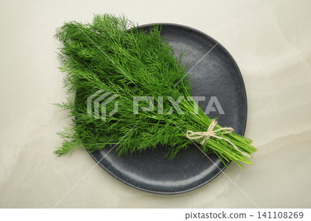 Bunch of green dill on dark plate on grey background. Bunch of green dill on dark plate on grey background. 141108269