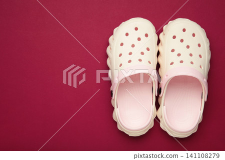 Mykolaiv, Ukraine - April 25, 2026: Couple of white Crocs sandals on dark red background. Mykolaiv, Ukraine - April 25, 2026: Couple of white Crocs sandals on dark red background. 141108279