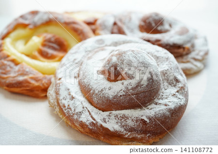 A delicious assortment of freshly baked Spanish ensaimadas topped with custard and powdered sugar. A delicious assortment of freshly baked Spanish ensaimadas topped with custard and powdered sugar. 141108772