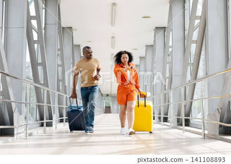 Young Black couple running through modern airport corridor with rolling suitcases Young Black couple running through modern airport corridor with rolling suitcases 141108893