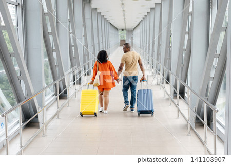 Rear view of Black couple holding hands while walking through modern airport Rear view of Black couple holding hands while walking through modern airport 141108907