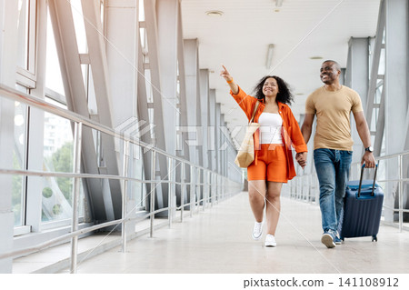 Black woman pointing excitedly while walking with partner through airport corridor 141108912