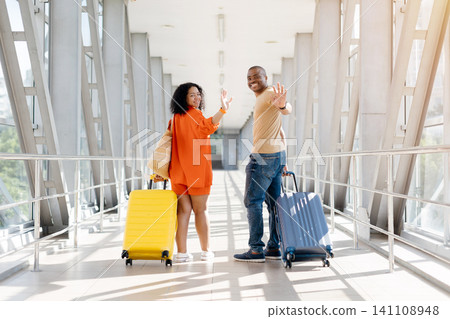 Happy black couple at airport terminal turning back and waving goodbye Happy black couple at airport terminal turning back and waving goodbye 141108948