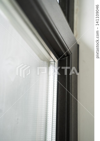 Window frame detail showing dark profile, glass, and texture, illustrating modern architecture and construction materials Window frame detail showing dark profile, glass, and texture, illustrating modern architecture and construction materials 141109046