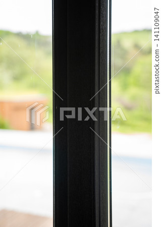 Black window frame creating a modern interior view overlooking a blurred outdoor pool and green landscape Black window frame creating a modern interior view overlooking a blurred outdoor pool and green landscape 141109047