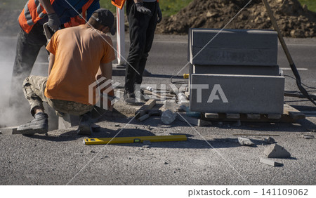 Road construction worker installing concrete curb using tools on city street with dust flying Road construction worker installing concrete curb using tools on city street with dust flying 141109062