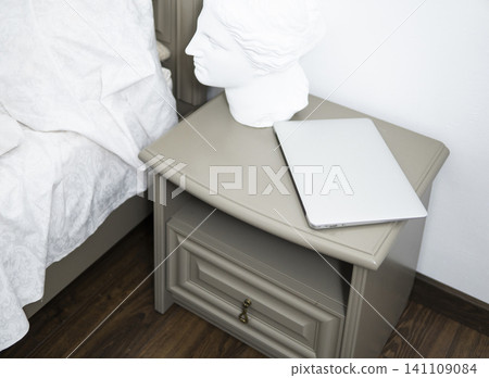Bedroom interior featuring classic sculpture bust next to modern laptop on contemporary nightstand 141109084