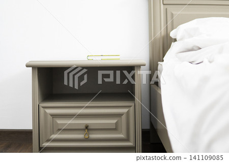 Nightstand with unread book next to bed, representing relaxation, comfort, and peaceful home living Nightstand with unread book next to bed, representing relaxation, comfort, and peaceful home living 141109085