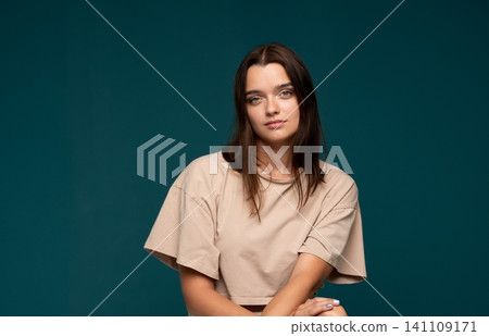 Young woman posing against a teal backdrop, radiating calm, natural beauty and quiet confidence in her casual fashion style 141109171