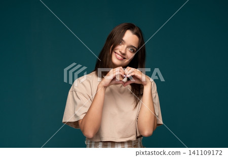 Young woman smiling and forming a heart shape with hands, expressing love, care, and happiness Young woman smiling and forming a heart shape with hands, expressing love, care, and happiness 141109172