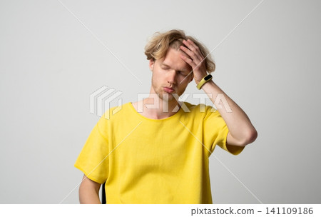 Young adult man experiencing headache with hand on forehead, feeling pain and discomfort, standing against a light background representing stress, fatigue, and illness Young adult man experiencing headache with hand on forehead, feeling pain and discomfort, standing against a light background representing stress, fatigue, and illness 141109186