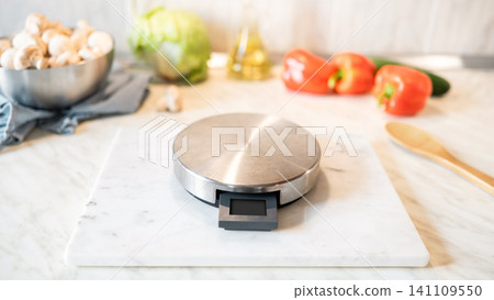 Kitchen scale on marble cutting board with vegetables healthy cooking concept Kitchen scale on marble cutting board with vegetables healthy cooking concept 141109550