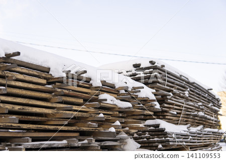 Wood planks and boards forming large stacks, covered with snow, stored outside for future building projects Wood planks and boards forming large stacks, covered with snow, stored outside for future building projects 141109553