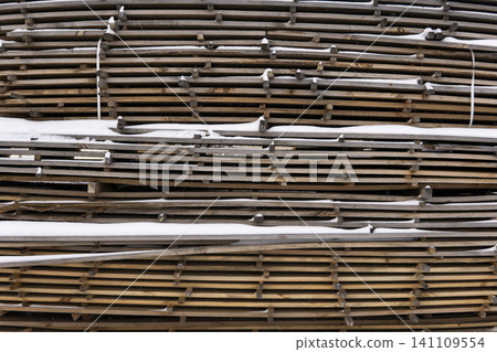 Stacked wooden boards and planks covered with a light layer of snow, representing a wood processing industry Stacked wooden boards and planks covered with a light layer of snow, representing a wood processing industry 141109554