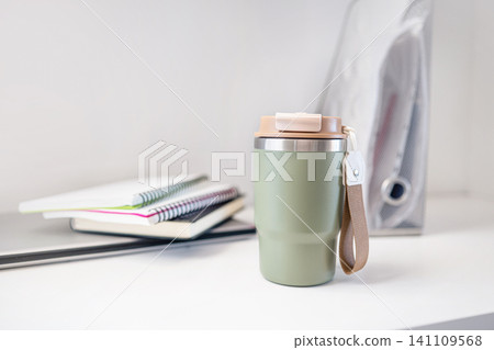 Reusable travel mug on workspace desk with notebooks minimal home office concept Reusable travel mug on workspace desk with notebooks minimal home office concept 141109568